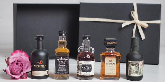 Five miniature bottles of Gin, Whisky, Rum and Disaronno in front of a gift box