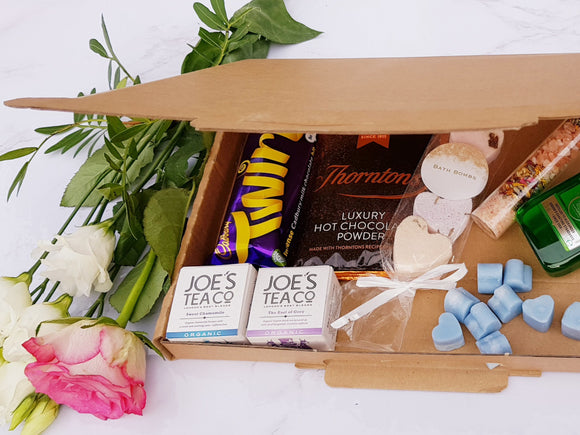 A letterbox friendly gift box showing contents of a Cadbury Twirl, a sachet of hot chocolate, bath bombs, bath salts, a bottle or Gordon's gin, some wax melts and two tea boxes