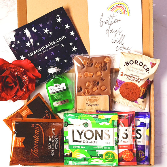 An opened gift box showing a packet of biscuits, a bottle of Gordon's gin, a slab of chocolate, a positivity print, two hot chocolate sachets, a trio of coffee and a self-heating eye mask