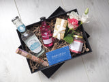 An opened gift box showing a bottle of tonic water, a bottle of Whitley Neill pink grapefruit gin, a box of chocolates, a scented candle and a tube of bath salts
