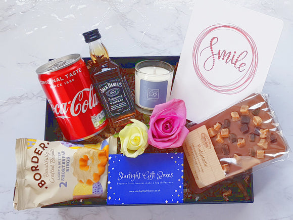 A gift box with a can of coke, a bottle of Jack Daniels whisky, a scented candle, a bar of handmade Belgium chocolate, a pack of biscuits and a card 