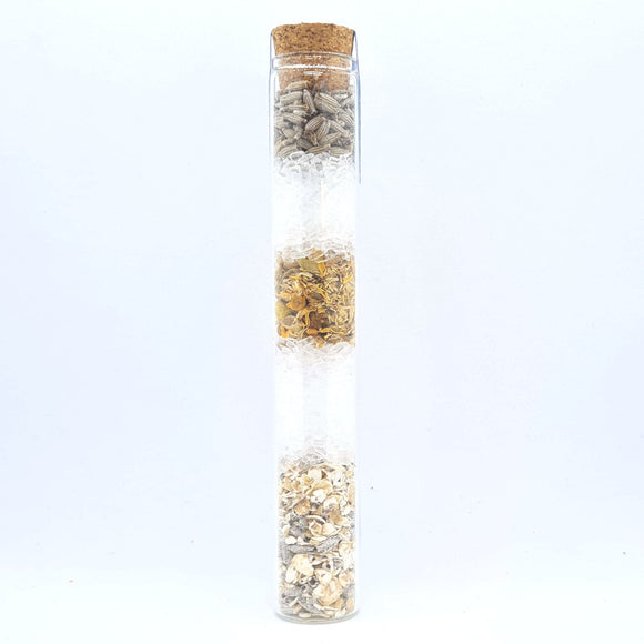 A glass tube containing white and grey layered bath salts with a cork lid