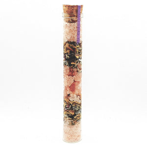 A glass tube containing pink and grey layered bath salts with a cork lid