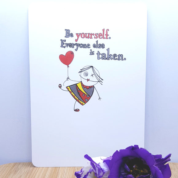 An A5 card showing a girl floating under a red heart shaped balloon with the words Be yourself. Everyone else is taken written on it, decorated with a purple flower in front