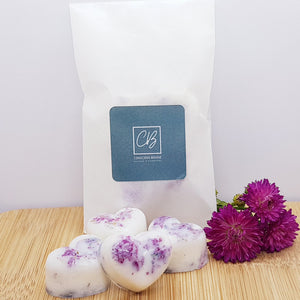 Four heart shaped wax melts in front of a biodegradable glassine packet