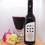 A bottle of Jack Rabbit Shiraz next to red wine in a glass, decorated with two flowers
