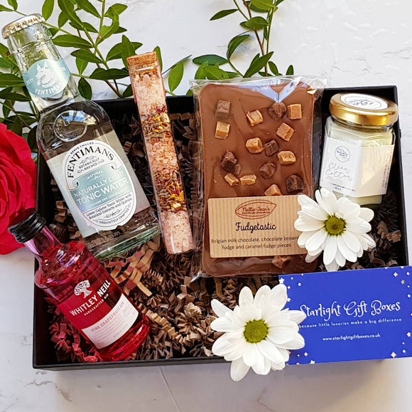 An opened gift box showing a bottle of tonic water, a bottle of Whitley Neill pink grapefruit gin, a handmade Belgian chocolate slab, a scented candle and a tube of bath salts
