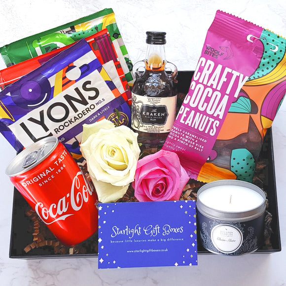 An opened gift box showing a bottle of Kraken rum, a can of Coke, a packet of cocoa powdered peanuts, a tin candle and a trio of coffee