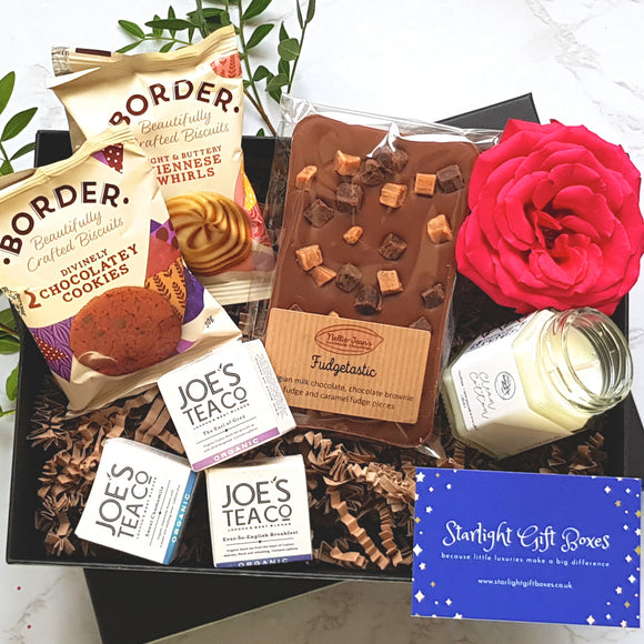 An opened gift box showing a packet of cookies, a packet of viennese whirls, a scented candle, three types of tea bags, and a handmade Belgian chocolate slab