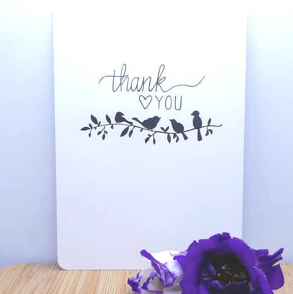 An A5 card showing silhouettes of birds on a branch with thank you written on it, decorated with a purple flower in front